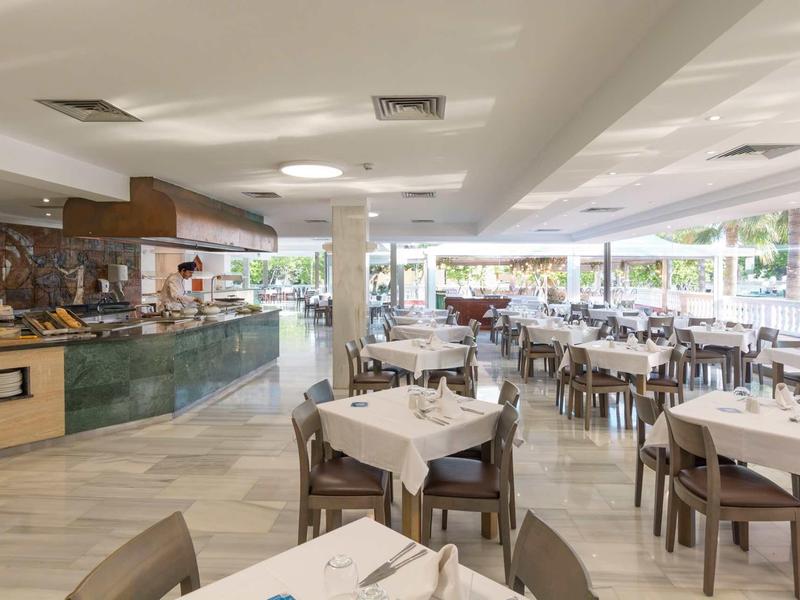 Großer heller Speisesaal mit vielen Tischen, weißen Tischdecken und Holzmöbeln in modernem Stil.