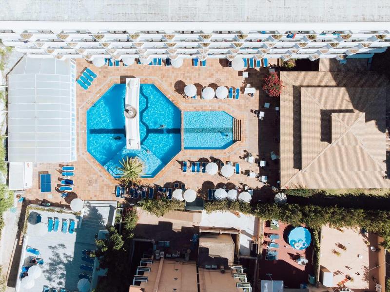 Luftaufnahme eines Hotels mit mehreren Pools, Sonnenliegen und einem großen rechteckigen Gebäude.