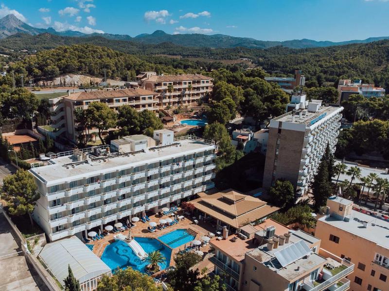 Mehrere Hotels mit Pools, umgeben von Bäumen und Hügeln unter blauem Himmel.