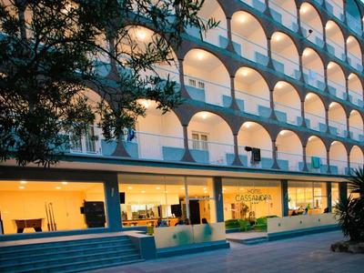 Edificio dell'hotel con balconi illuminati al crepuscolo e vegetazione circostante.