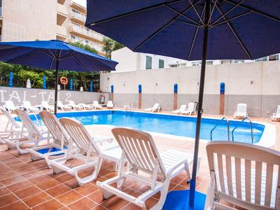 Area piscina di un hotel con sdraio bianche e ombrelloni blu su una terrazza.