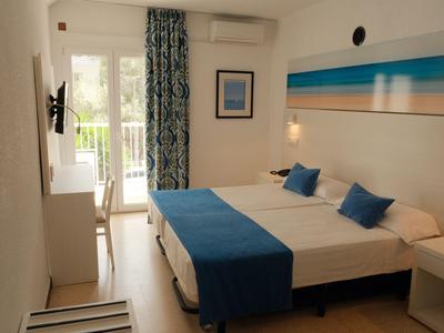 Licht ingericht hotelkamer met tweepersoonsbed, blauwe accenten en balkon met uitzicht op groen.