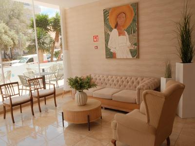 Lichte hotellobby met beige zitmeubilair, groot raam, planten en een portret aan de muur.