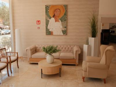 Lichte hotellobby met beige banken, ronde poefs en kunstwerk aan de muur bij grote ramen.
