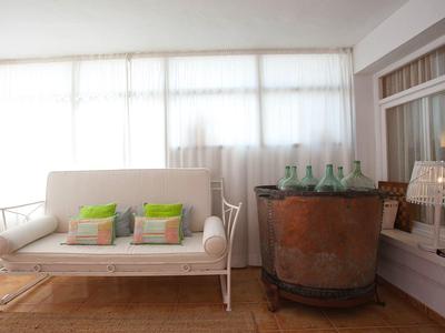 Jasne pomieszczenie z przytulną białą sofą i dużą antyczną donicą z zielonymi szklanymi butelkami