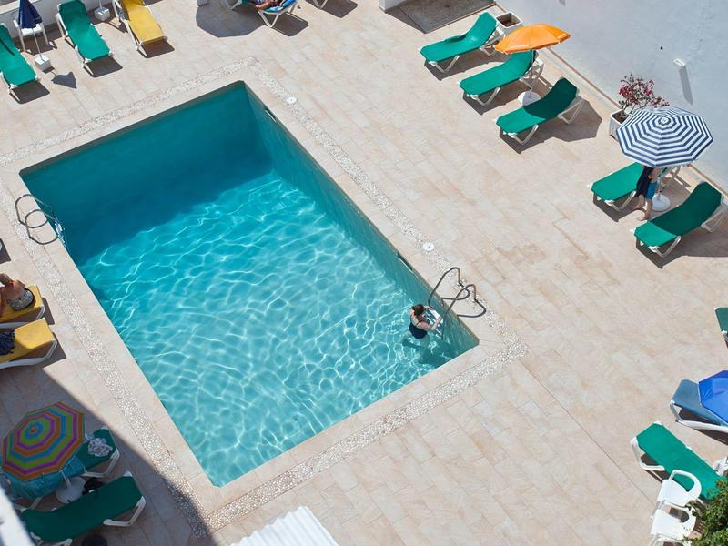 Widok na prostokątny basen z leżakami i kolorowymi parasolami na tarasie.