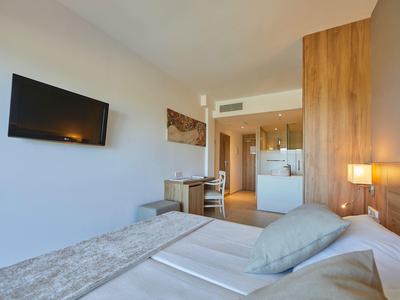 Habitación de hotel moderna con cama doble, televisor en la pared y detalles de madera que complementan el diseño luminoso.