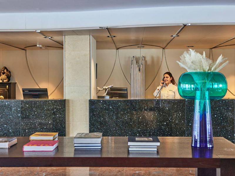 Mostrador de recepción de un hotel con una empleada al fondo y un arreglo floral al frente.