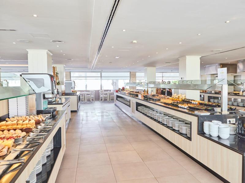 Amplio comedor de desayuno de hotel con buffet, variedad de alimentos y ventanas panorámicas.