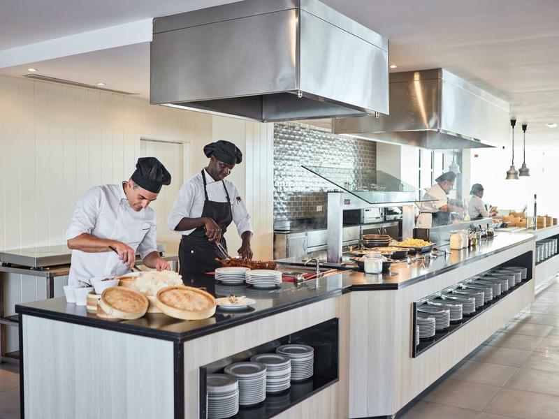 Cocina moderna de hotel con chefs preparando comida y utensilios organizados en la barra.