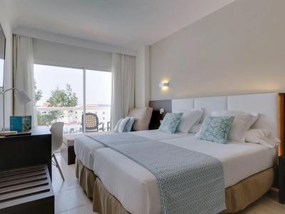 Camera d'hotel luminosa con letto matrimoniale, comodini, scrivania e balcone con vista esterna.