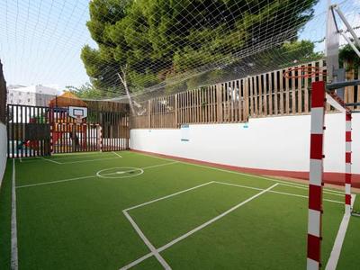 Piccolo campo sportivo all'aperto con prato verde artificiale e tetto in rete accanto a un edificio dell'hotel.