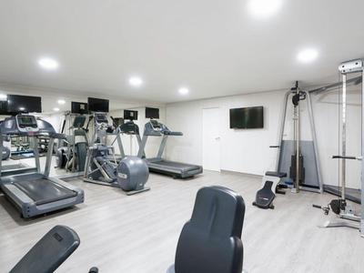 Nowoczesna siłownia z bieżniami, trenażerami eliptycznymi i wielofunkcyjnym sprzętem w jasnym pomieszczeniu.