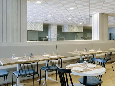 Ristorante luminoso e moderno con più tavoli, sedie e pareti bianche.