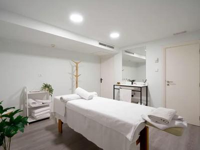 Stanza trattamento luminosa con lettino da massaggio, asciugamani e piante per un'atmosfera rilassante.