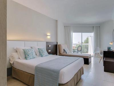 Helles Hotelzimmer mit Doppelbett, Sitzbereich und Balkon mit Ausblick.