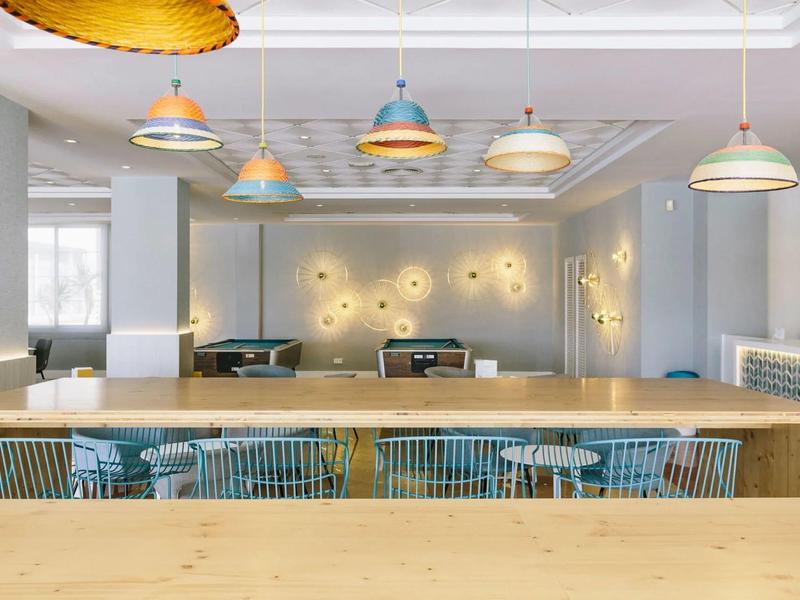 Area pranzo moderna con tavolo in legno, sedie colorate e luci da soffitto di design.