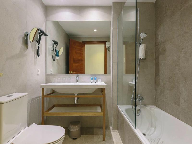 Bagno moderno con WC, lavabo, specchio e vasca da bagno con parete doccia.