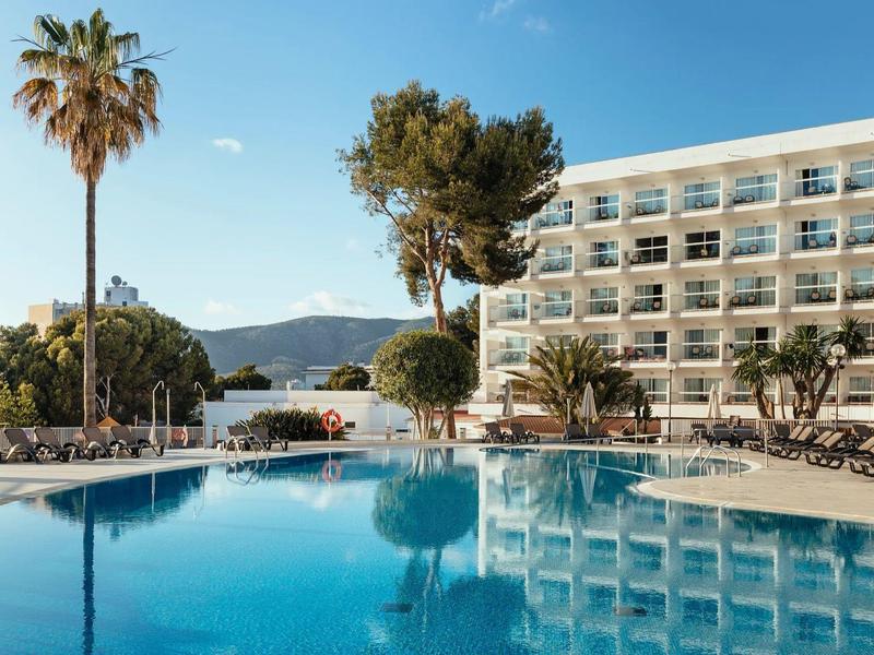 Hotel con grande piscina, palme e camere con balcone sotto un cielo limpido.