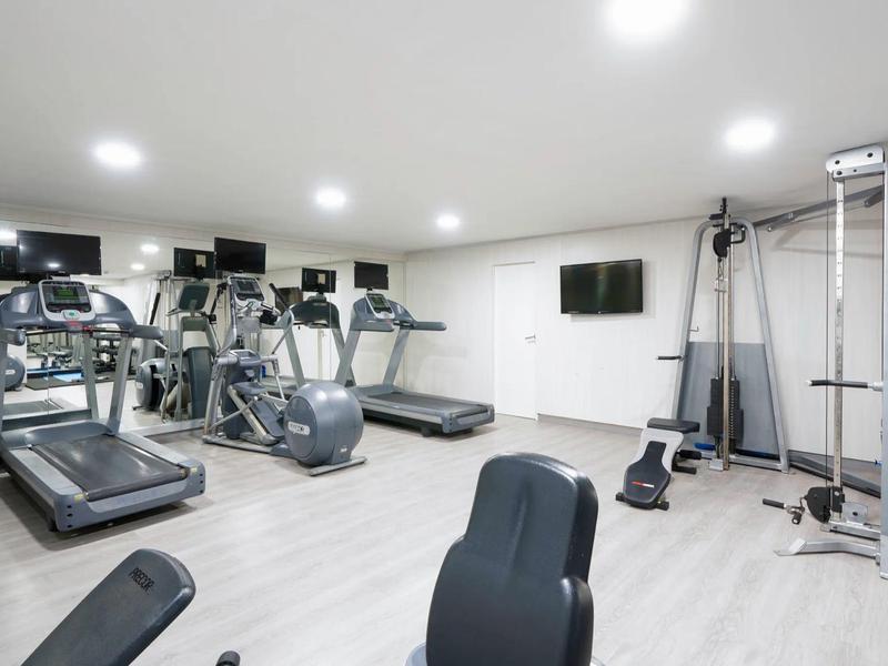 Palestra moderna con tapis roulant, ellittiche e attrezzi per la forza in una stanza luminosa.