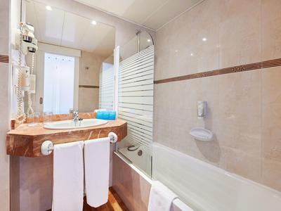 Bagno luminoso con lavabo, specchio, vasca da bagno e asciugamani bianchi.