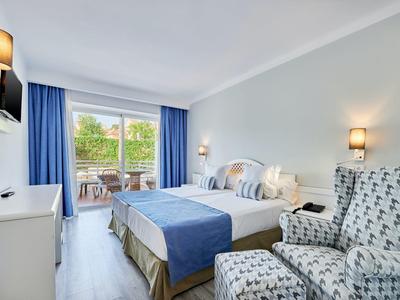 Camera d'hotel moderna con letto matrimoniale, poltrone, balcone e vista verde.