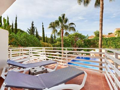Balcone con due sdraio, ringhiera bianca e vista su palme e piscina.