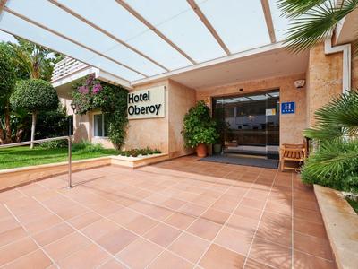 Area d'ingresso dell'Hotel Oberoy con pensilina in vetro e spazio esterno curato.