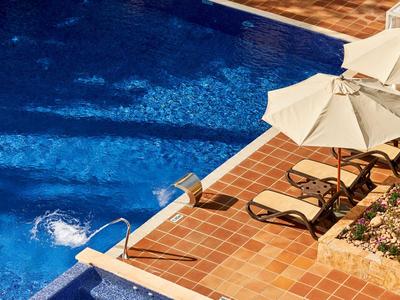 Blauer Pool mit Terrakottafliesen und Sonnenschirmen neben Liegestühlen.