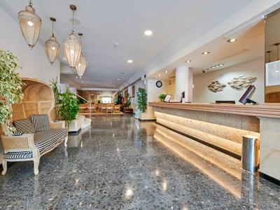 Moderna hall d'hotel con reception, aree salotto e piante.