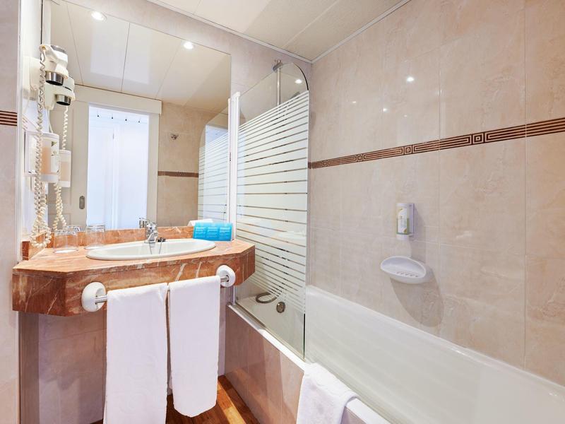 Bagno luminoso con lavabo, specchio, vasca da bagno e asciugamani bianchi.