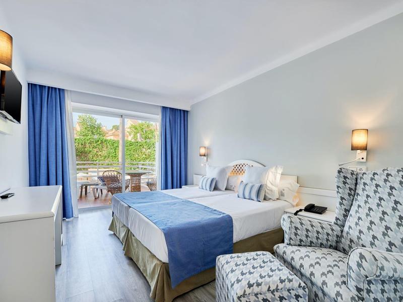 Camera d'hotel moderna con letto matrimoniale, poltrone, balcone e vista verde.