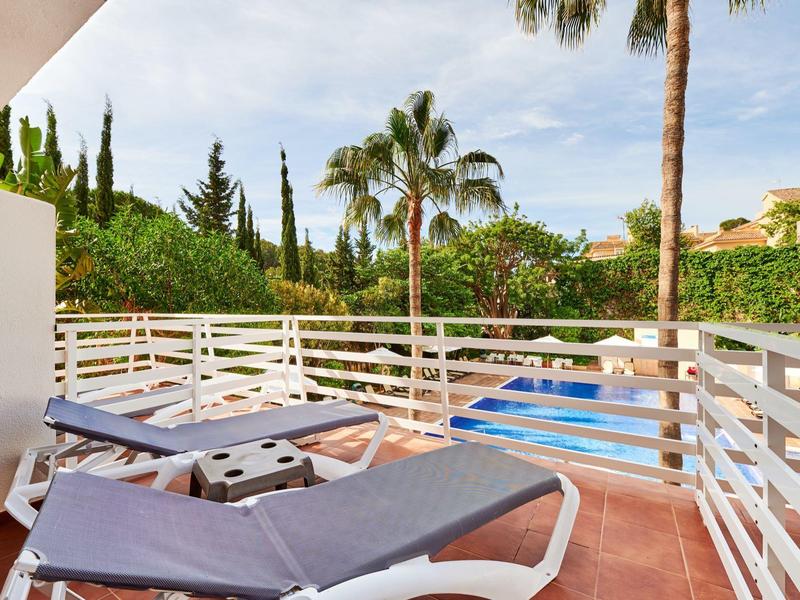 Balcone con due sdraio, ringhiera bianca e vista su palme e piscina.