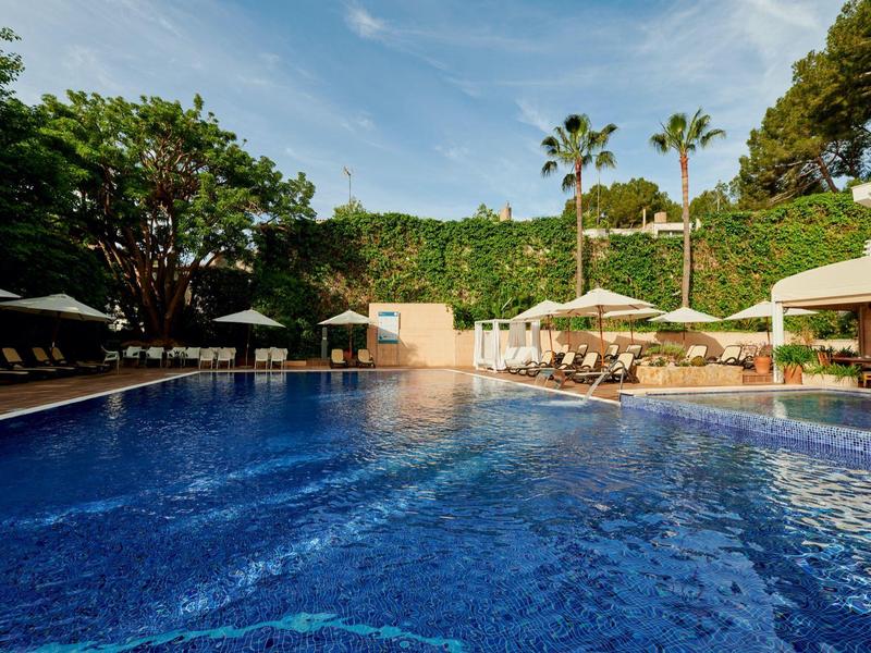 Piscina blu con lettini e palme in un'area alberghiera soleggiata.