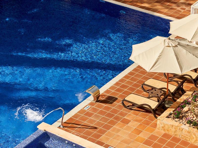 Piscina blu con sdraio e ombrelloni accanto a pavimento in terracotta