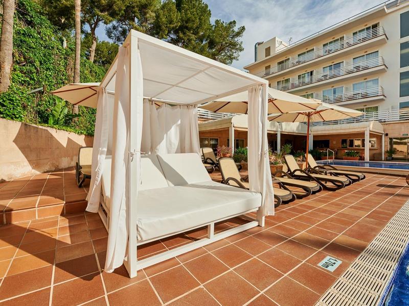 Gazebo con letto lounge ombreggiato accanto a una piscina con lettini su una terrazza