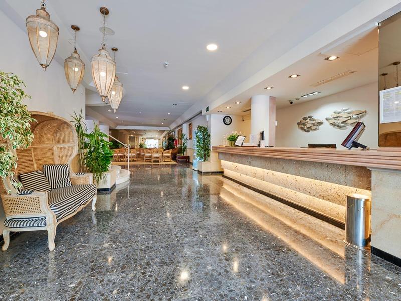 Moderna hall d'hotel con reception, aree salotto e piante.