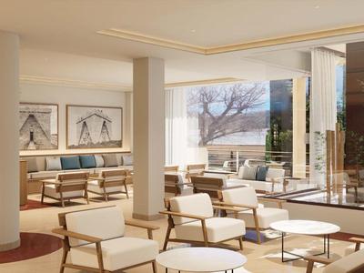 Jasny hotelowy salon z wygodnymi fotelami, stolikami i dużymi oknami z widokiem na drzewa.