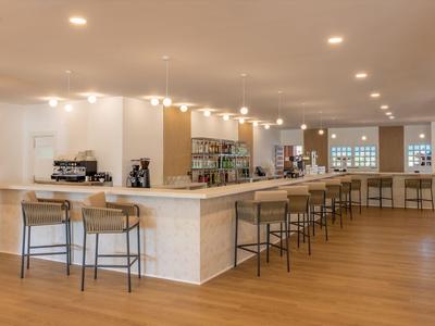 Moderner Hotelbarbereich mit langem weißen Tresen und Holzstühlen auf hellem Parkettboden.
