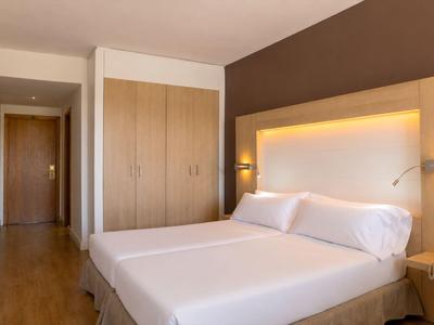 Helles Hotelzimmer mit Doppelbett, Nachttischen und einem großen Kleiderschrank.