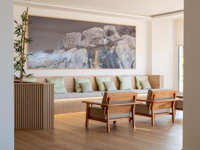 Modern eingerichteter Hotel-Wartebereich mit Holzstühlen, Sofa und großem Kunstwerk an der Wand.
