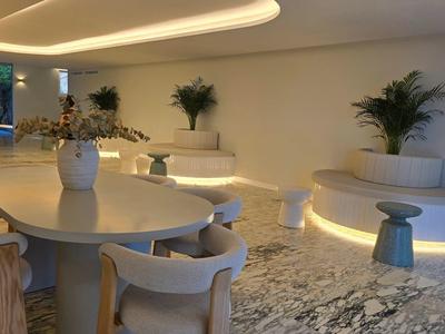 Espace lounge moderne d'hôtel avec tables rondes, chaises blanches et éclairage indirect.