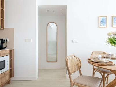 Salle à manger lumineuse avec chaise en bois, table ronde et miroir en arc au mur