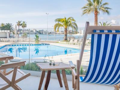 Blick von einer Terrasse auf einen Pool mit Liegestuhl und Blick auf das Meer und Palmen.