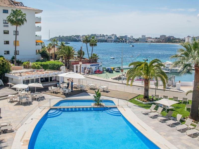 Piscine d'hôtel avec chaises longues et vue sur la mer et la ville côtière.