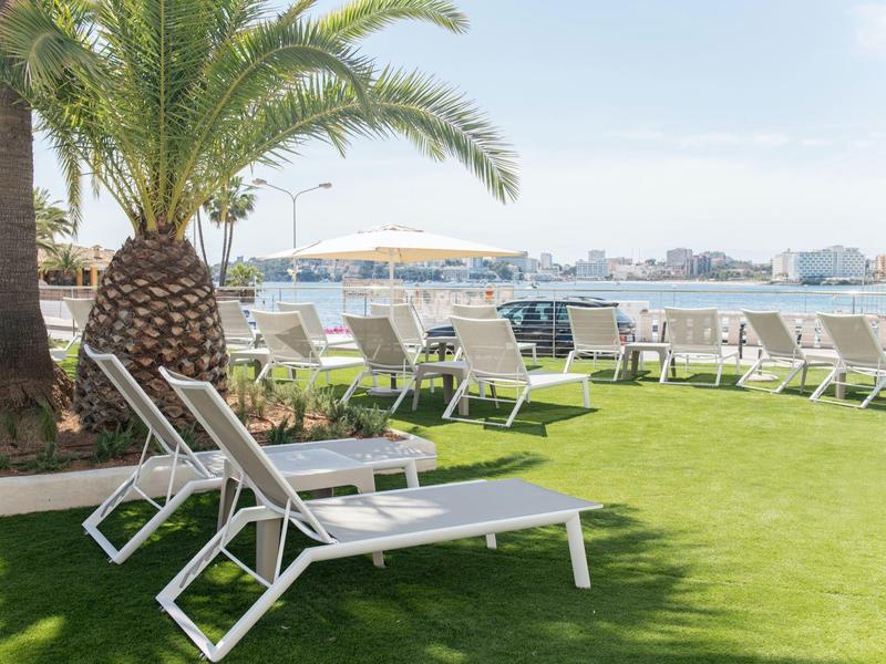 Chaises longues sur herbe verte avec vue sur la mer et une ville en arrière-plan.