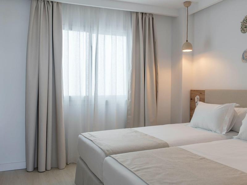 Chambre d'hôtel simple avec deux lits, murs blancs et lampe de chevet allumée.