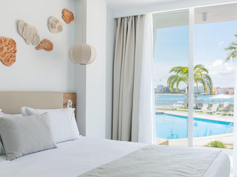 Chambre lumineuse décorée avec vue sur une piscine et des palmiers à travers de grandes fenêtres
