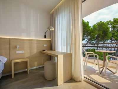 Modernes Hotelzimmer mit Balkon, Blick auf Bäume und Meer, helle Vorhänge und minimalistische Möbel.