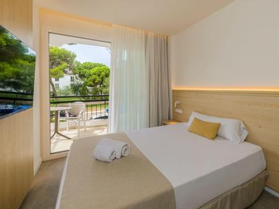 Modernes Hotelzimmer mit Doppelbett, Balkon und Blick auf grüne Bäume.